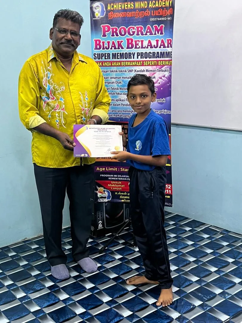 AMA student receiving recognition beside a Bijak Belajar programme banner
